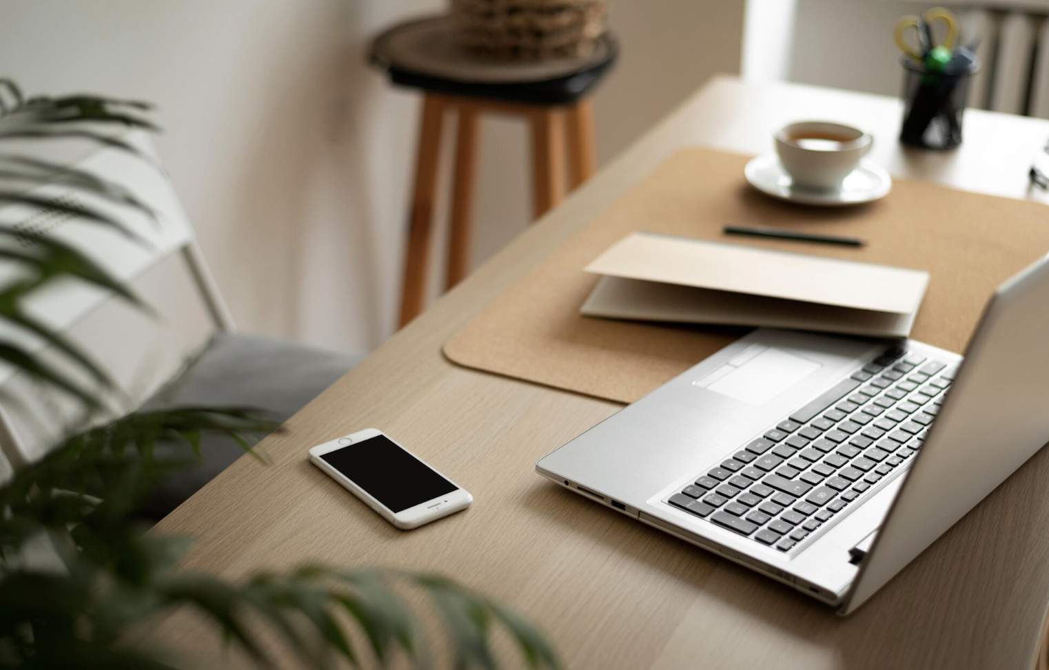 modern-graphic-designer-workspace Minimalist graphic designer’s workspace with laptop, coffee cup, smartphone, and notebook on a light wood desk.